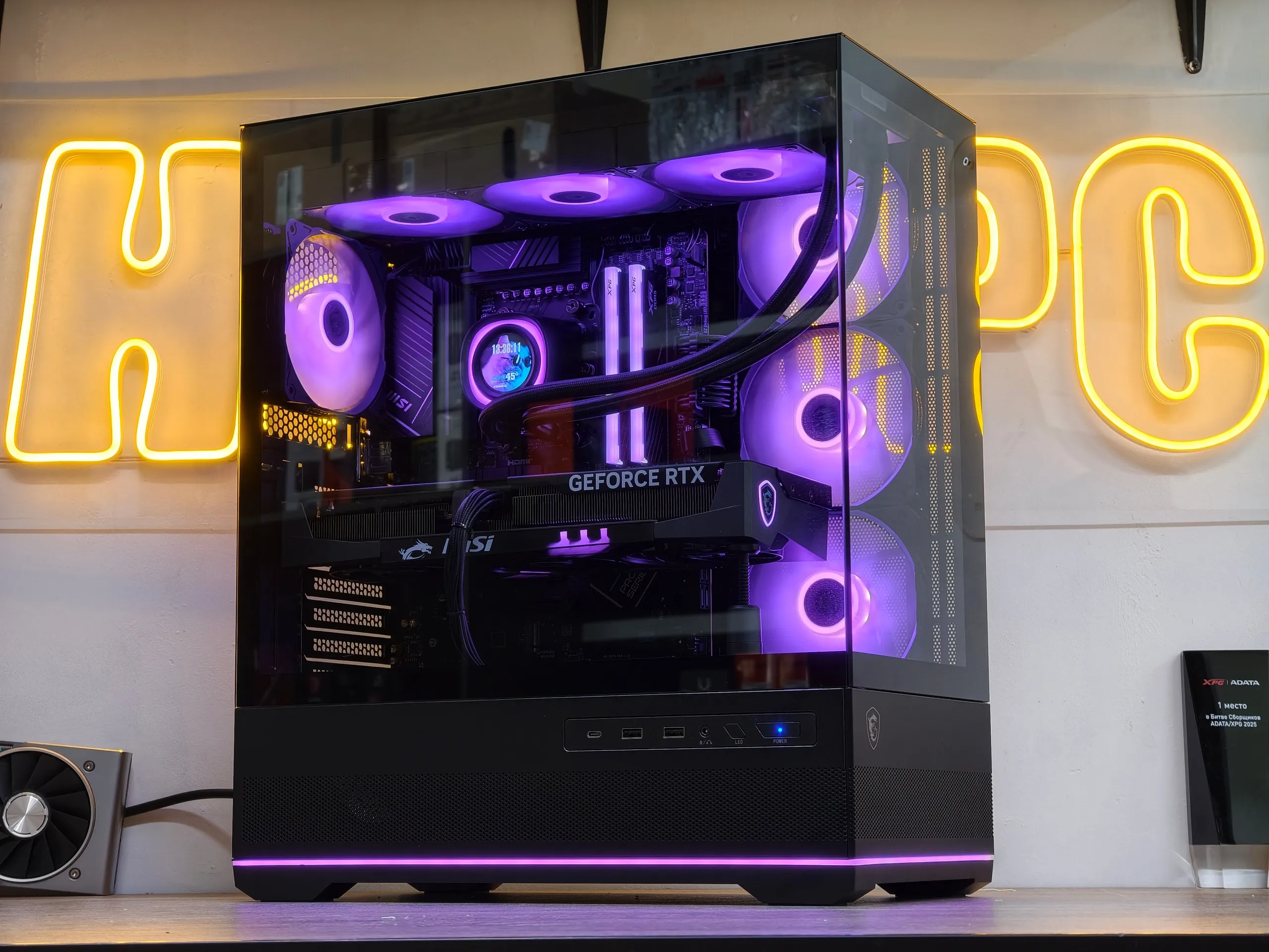 Игровая сборка HappyPC с СЖО и фиолетовой подсветкой на фоне неоновой вывески мастерской